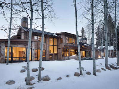 Modern ranch-style home with large windows, wooden exterior, and snow-covered surroundings.